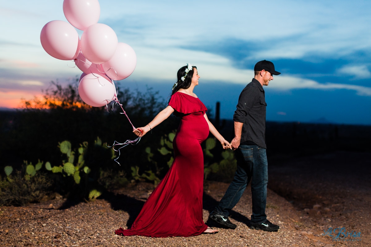 pink balloons red maternity dress walking through desert